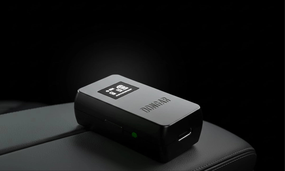Dongar Classic+ adapter with its OLED display lit, resting on a car armrest