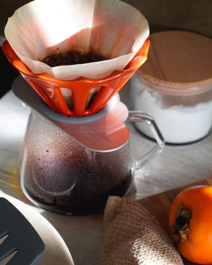 Orange ceramic Dotyk dripper brewing coffee into a glass carafe
